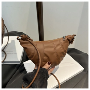Macro shot of brown croissant bag featuring vertical pleats and silver zipper detail