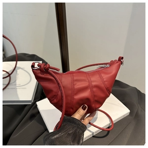 Detail of burgundy crescent crossbody bag featuring vertical quilting and knotted strap design