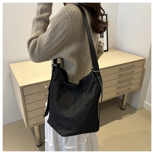 Détail d'un sac seau noir texturé avec bandoulière en cuir et boucle argentée sur modèle