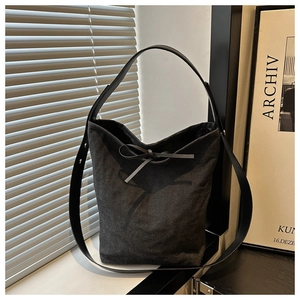 Detail of grey canvas bucket bag with bow tie and leather strap in an artistic setting