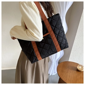 Quilted tote bag with contrast brown shoulder strap shown on a model in a minimal interior
