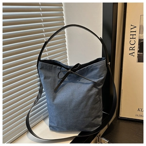Detail of blue denim bucket bag with black leather strap and bow tie closure
