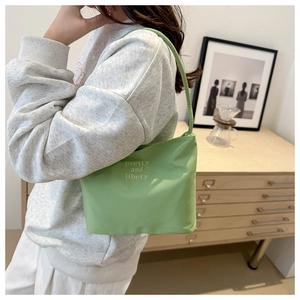 Close-up of light green shoulder bag with white embroidery worn by a model in casual style