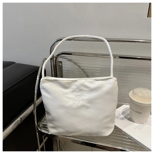 Close-up of white bucket bag with pretty and libety embroidery on minimal shelf