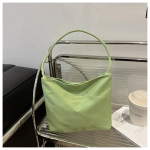 Close-up of light green canvas tote bag featuring yellow 'pretty and liberty' embroidery