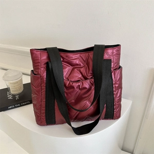 Burgunderrote gesteppte Tragetasche aus glänzendem Nylon mit Taschen auf weißem Podest