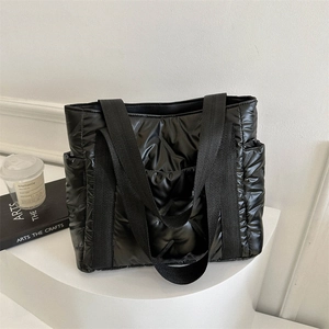 Schwarze gesteppte Puffer-Tasche mit Bandgriffen auf weißem Podest präsentiert