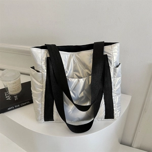 Silberne Stepp-Tote-Bag mit schwarzen Tragegurten und Seitentaschen auf weißem Pult