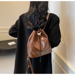 Sac à dos seau marron brillant avec boucle papillon porté sur manteau noir