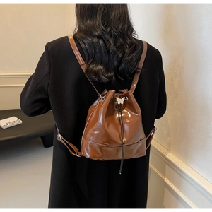 Detail of a brown glossy leather drawstring backpack with a white butterfly ornament