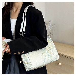 Close-up of bamboo leaf embroidery on tote bag with white leather straps and metal rings
