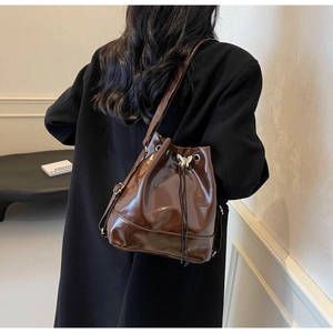 Detail of a brown glossy bucket bag with a silver butterfly buckle and drawstring closure