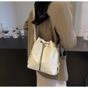 Detail of cream drawstring bucket bag with silver butterfly charm and adjustable strap