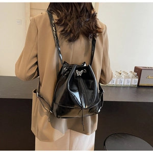 Model wearing a black glossy drawstring backpack with elegant silver butterfly buckle detail