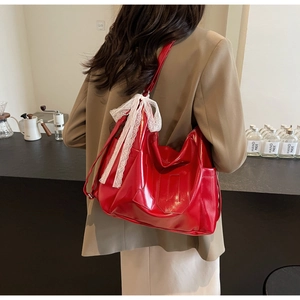 Detail of red patent leather hobo bag with a white lace bow charm on model back