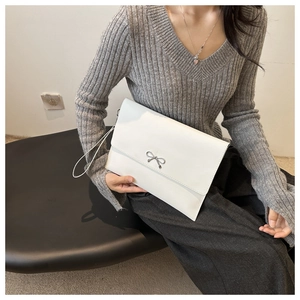 Close-up of white leather envelope clutch featuring a delicate silver bow metal clasp