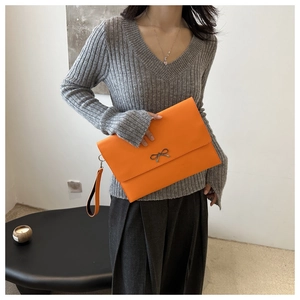 Nahaufnahme der leuchtend orangefarbenen Briefumschlag-Clutch mit goldener Schleife