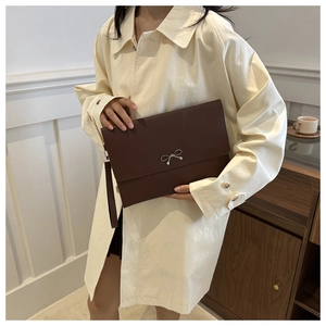 Detail einer dunkelbraunen Umschlag-Clutch mit silberner Schleife und Lederband