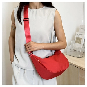 Detail of red crescent crossbody bag featuring adjustable wide strap and nylon texture