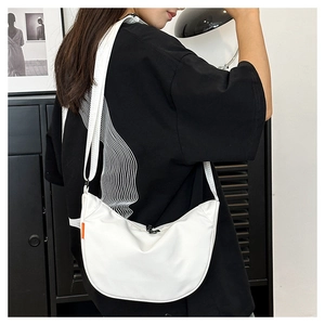 Detail view of the white crescent crossbody bag on a model showing strap and nylon fabric