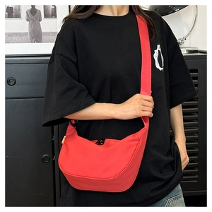 Close-up of a red nylon crescent moon crossbody bag with wide shoulder strap on model