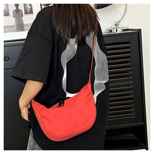 Rear view of minimalist bright red nylon dumpling crossbody bag worn over a black shirt