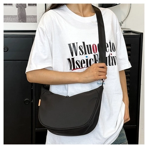 Detail of a black crescent crossbody bag worn by a model in a casual indoor setting
