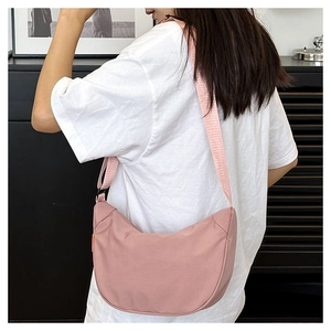 Pink crescent nylon crossbody bag worn by model in a minimalist home setting