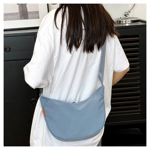 Detail of blue nylon crescent bag featuring a casual crossbody strap and orange side label