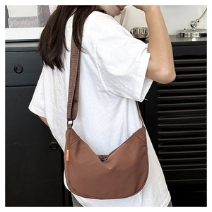 Brown nylon crescent bag detail showing wide strap and orange tag on model