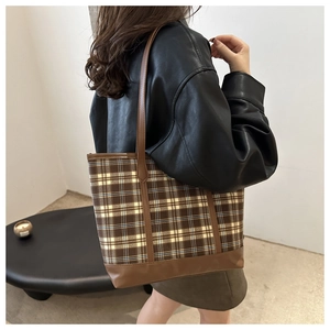 Detail of tartan pattern tote bag with brown leather straps shown on model shoulder