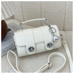 Detail of cream faux crocodile texture handbag with dual metal locks on a plush sofa
