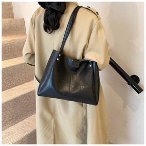 Classic black PU leather tote bag with gold rivets and dual straps shown on shoulder