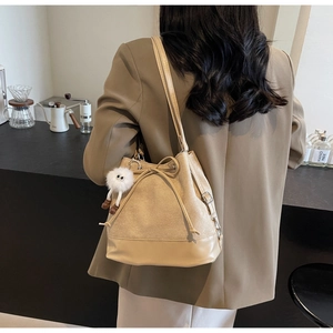 Detail of beige bucket shoulder bag with drawstring and plush charm on brown blazer