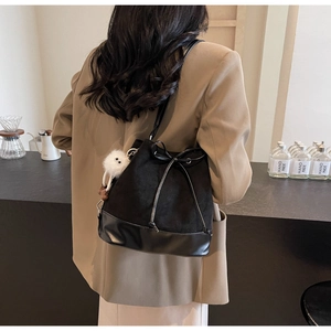 Detail of black bucket bag with bow drawstring and white plush eye charm accessory