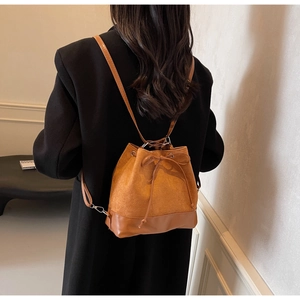 Brown drawstring bucket backpack in suede and leather mix worn by a model in a room