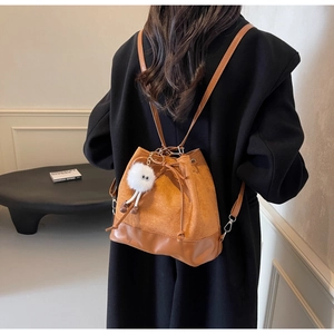 Detail of a brown suede drawstring backpack with a cute white plush doll keychain charm