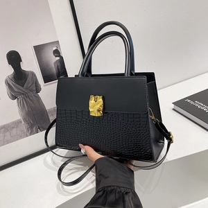 Fashionable black crocodile texture handbag with gold metal clasp on a white table