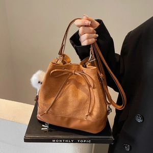 Brown faux suede bucket bag with drawstring bow and plush charm on black books