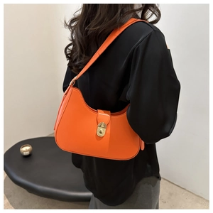Detail of a bright orange hobo bag with a gold oval metal twist lock and smooth texture