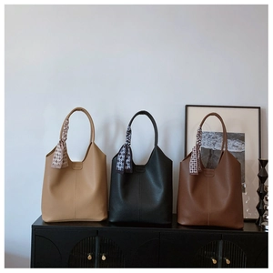 Three minimalist tote bags in khaki, black, and brown with silk scarves on a cabinet