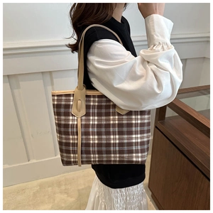 Detail of a brown plaid tote bag featuring leather straps on a casual female model