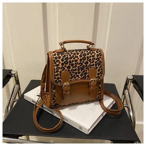 Detail of leopard print backpack with gold buckles and handle on a white book
