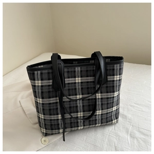 Detail of classic plaid tote bag with black leather straps and premium woven texture