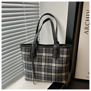 Detail of checkered canvas tote bag with black leather straps against a minimalist window