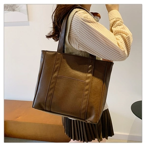 Detail of a large dark brown PU leather tote bag with vertical decorative stitching