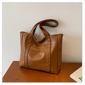 Detailed view of brown leather tote bag with wide straps on a wooden surface