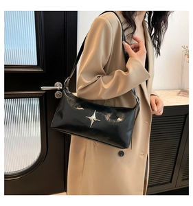 Detail of minimalist black faux leather shoulder bag featuring a silver star ornament