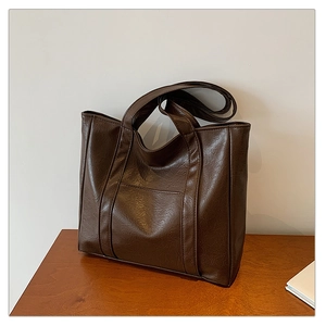 Detail of dark brown faux leather tote bag with vintage texture on a wooden desk