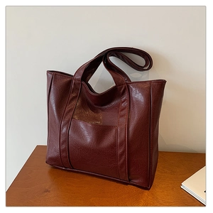 Detail of burgundy tote bag with glossy wrinkled leather texture on a wooden surface